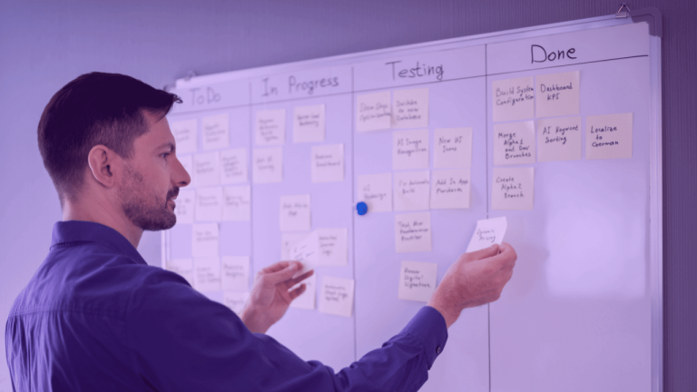 A imagem mostra um homem em frente a um quadro Kanban, ajustando os post-its em seus respectivos quadros. A foto ilustra como