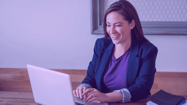 A imagem mostra uma mulher sorrindo para o computador. A foto sugere que ela está se preparando para uma migração de carreira