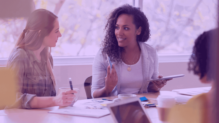 A imagem mostra duas mulheres conversando no ambiente de trabalho, o que sugere que elas estão construindo um plano de ação c