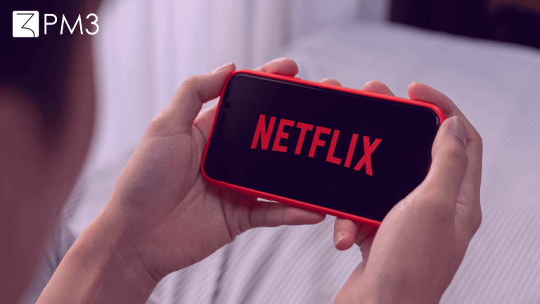 A imagem mostra um par de mãos segurando um celular que exibe a logo da Netflix